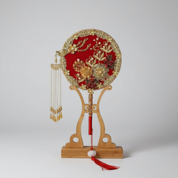 Decorative fan with intricate designs on a wooden stand against a dark background